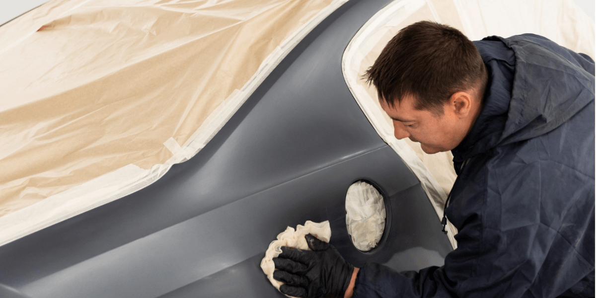 A man carefully paints a car using a white cloth to protect the surrounding area from paint splatters.